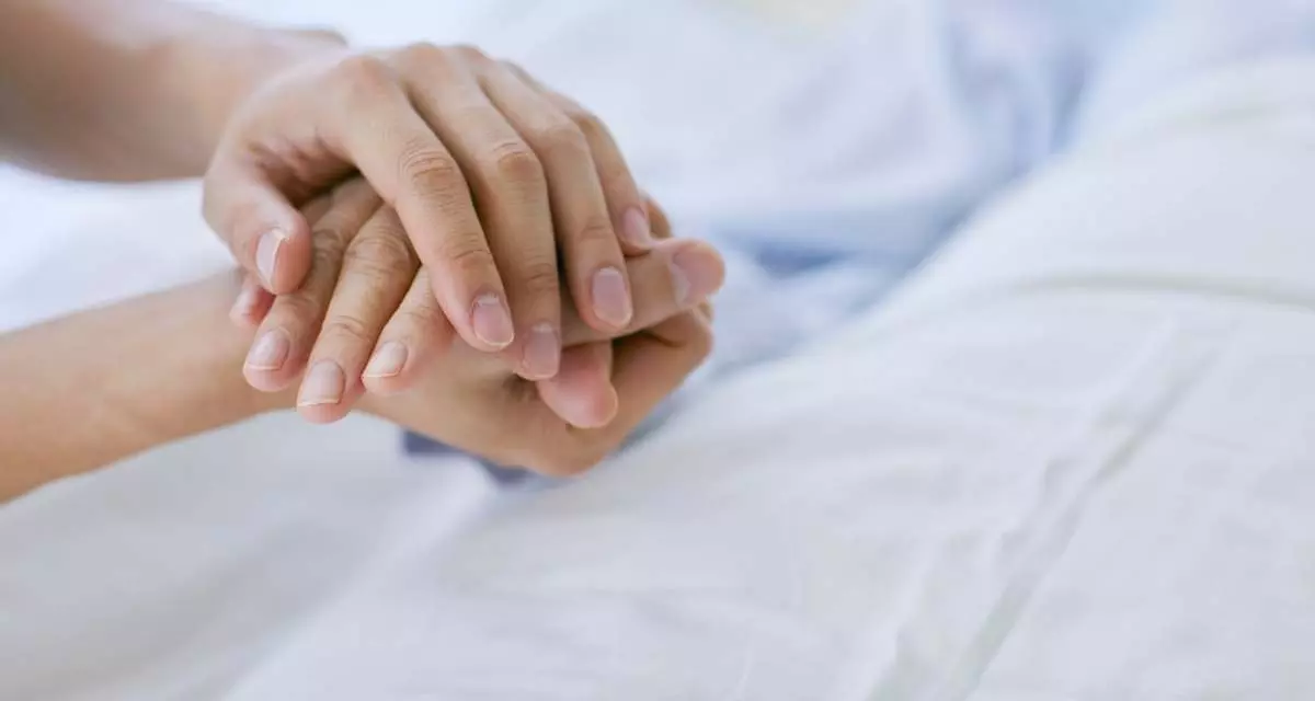 Pflege Symbolbild. Foto: Canva | Aflo Images Junge Hände halten eine alte Hand vor weißer Bettwäsche.