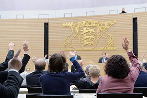 Abgeordnete heben die Hand, im Hintergrund das Staatswappen Baden-Württembergs