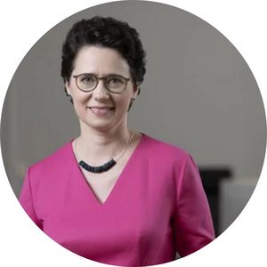 Potrait von Marion Gentges. Sie hat dunkle Haare, eine Kurzhaarfrisur und trägt eine Brille und eine Kette zu ihrem pinken Oberteil.