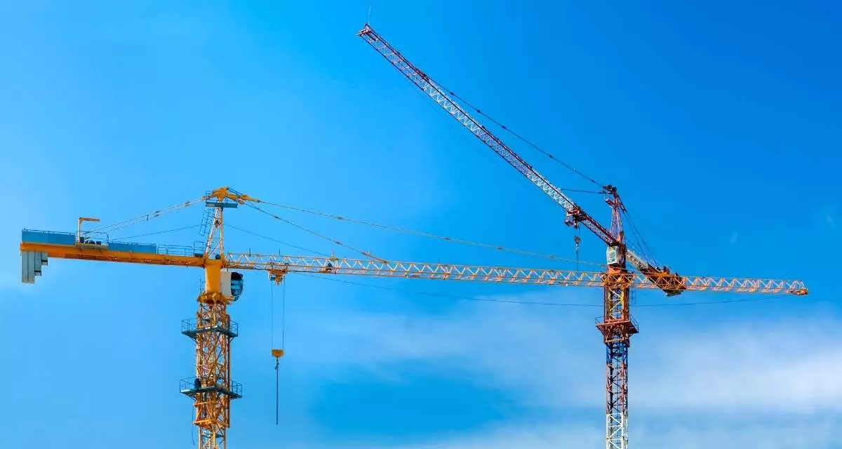 Symbolbil Bauen. Foto: Canva | DariolaVera Zwei Baukräne vor blauem Himmel.