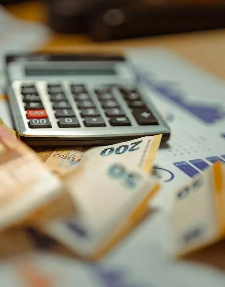 Foto von Geldscheinen, einem Taschenrechner und ausgedruckten Grafiken auf einem Tisch.