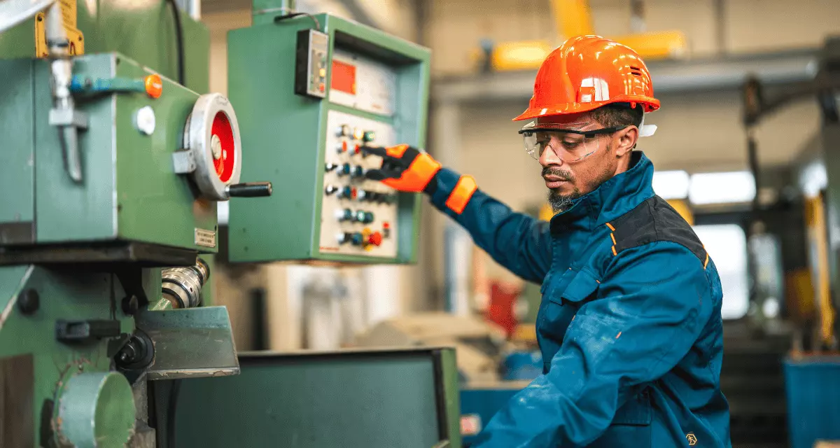 Eine Person im Blaumann mit roten Schutzhelm an einer Maschine.